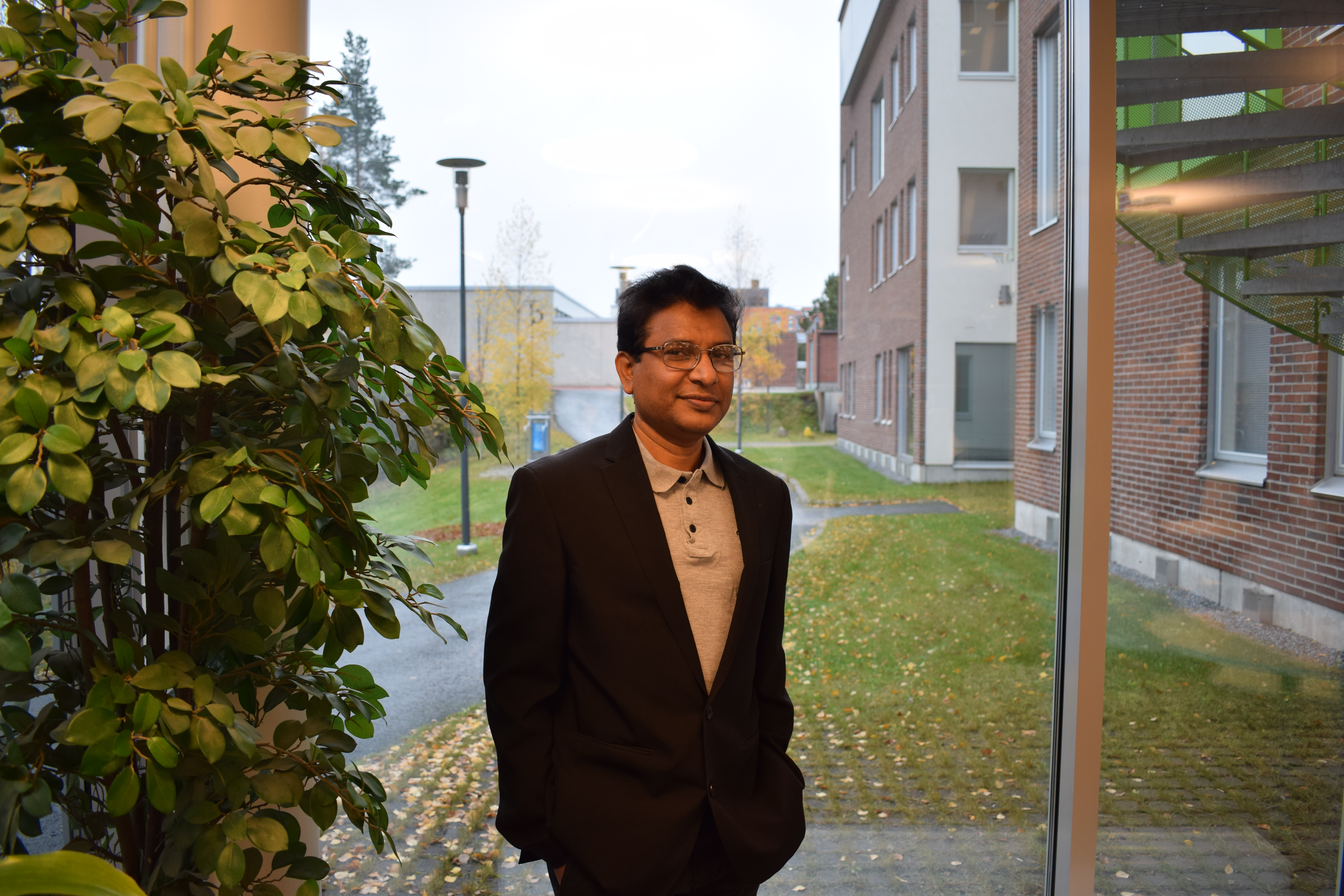 SM Shafiqul Alam seisoo ikkunan edessä ja hänen vieressään vasemmalla on suuri huonekasvi.